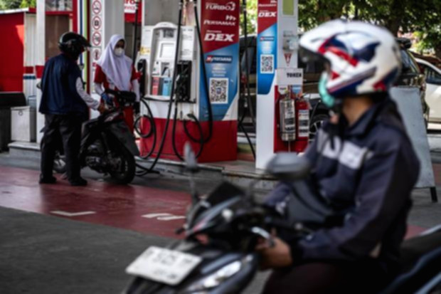 Papan informasi harga bahan bakar minyak di SPBU Pertamina dengan latar belakang suasana jalan raya.